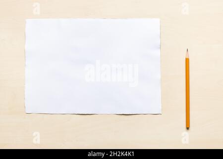 top view of wooden pencil near blank sheet of white textured watercolour paper on light brown wooden board Stock Photo