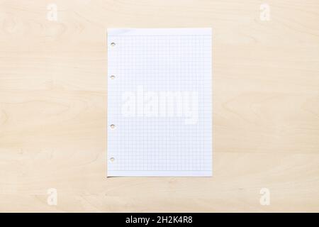 top view of blank sheet of squared paper on light brown wooden board Stock Photo