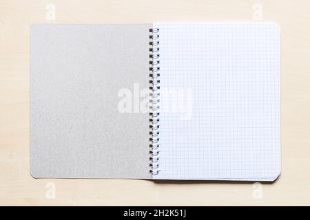 top view of first squared page of open blank spiral notebook on light brown wooden board Stock Photo