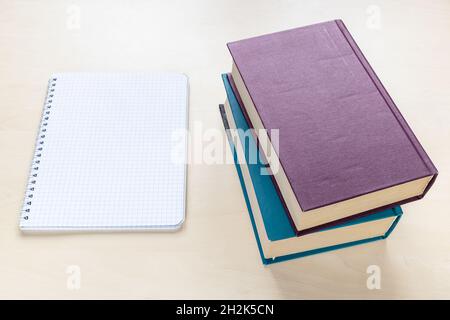 above view of two thick books and blank spiral notebook with squared paper on light brown wooden board Stock Photo