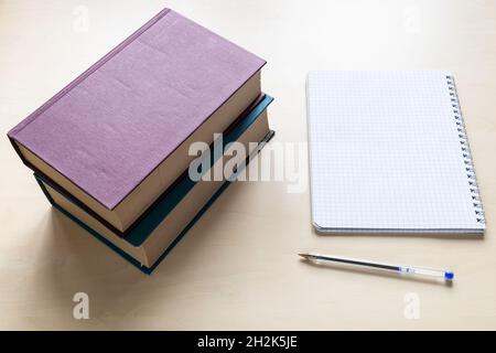 above view of two thick books, pen and blank spiral notebook with squared paper on light brown wooden board Stock Photo