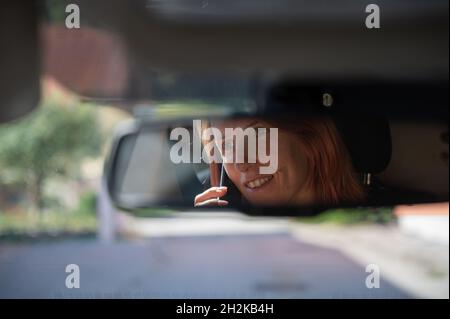 Photo of a woman in rearview mirror in the car recklessly talking on her mobile phone while driving. Stock Photo