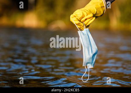Volunteer is picking up disposable used face mask from polluted water. Global environmental issues after covid-19 pandemic. Water pollution Stock Photo