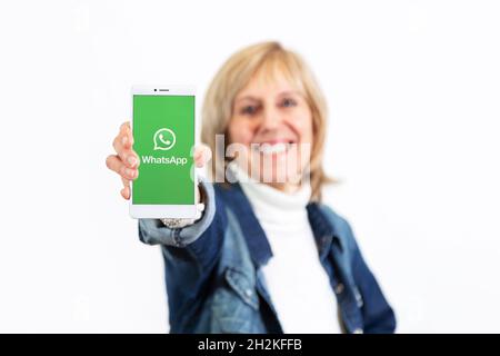 Happy woman over white background showing a smartphone with whatsapp logo on the screen. ROSARIO, ARGENTINA - OCTOBER 22, 2021 Stock Photo