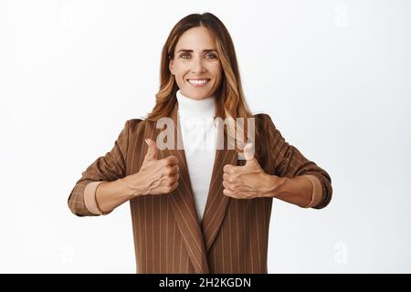 Business people. Smiling corporate woman showing thumbs up and looking pleased, give permission, compliment good quality, white background Stock Photo