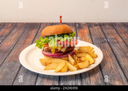 Crispy chicken burger with melted Emmental cheese, red onion, lettuce and tomato, mustard sauce and French fries in wedges Stock Photo