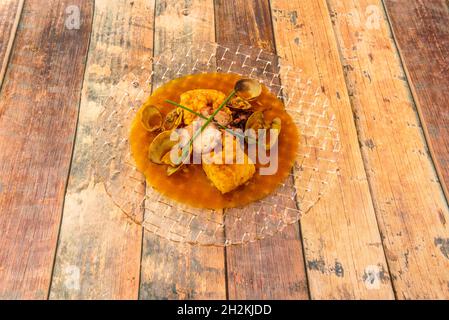 Nice transparent glass dish with Spanish stew of hake casserole with seafood. Cooked octopus, prawns and clams with chives Stock Photo