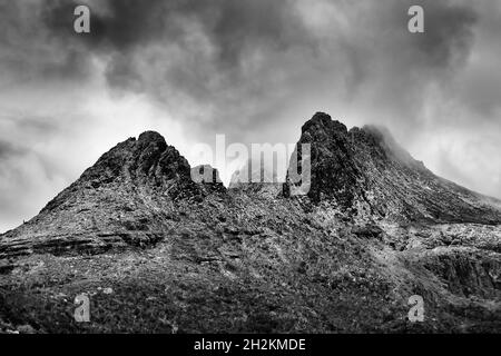 Dramatic black-white impression of aged rugged peaks of Cradle Mountain in Tasmania catching clouds. Stock Photo