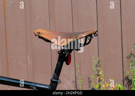 Brown leather bicycle saddle against a brown painted wooden fence. Ottawa, ON, Canada Stock Photo