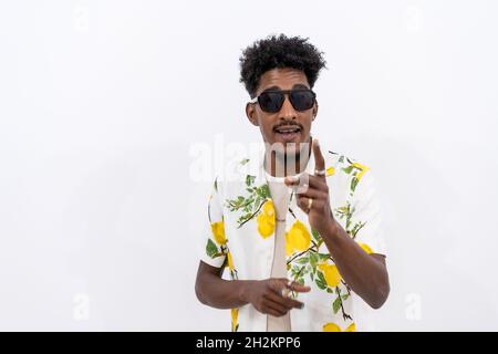 Young Cuban male in a floral shirt and black sunglasses dancing on a white background Stock Photo