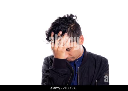 Disappointed man with his hand on his face. White background. Disappointed or embarrassed young latino man placing his hand on face. Stock Photo