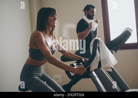 Determined young couple working out in gym. Fit boy and girl doing exercise with cyclette and tapis roulant. Beautiful sporty woman. Strong boys works Stock Photo