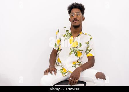 Young Cuban man in floral shirt and sunglasses sitting and posing on a white background Stock Photo