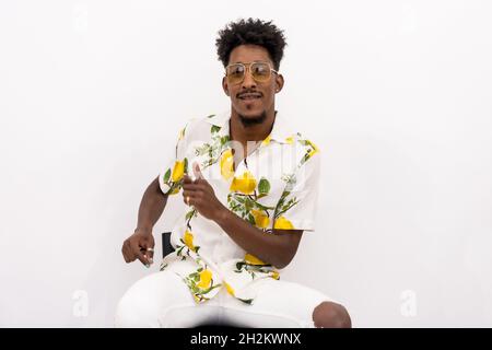 Young Cuban male in a floral shirt and sunglasses smiling and dancing on a white background Stock Photo