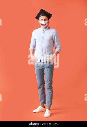 Male graduating student wearing medical mask with drawn smile against color background Stock Photo