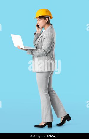 Female industrial engineer with laptop talking by mobile phone on blue background Stock Photo