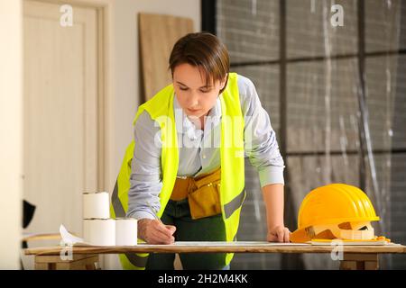 Female construction worker writing on house plan in room Stock Photo