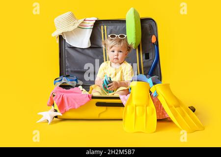 Cute baby girl in suitcase with belongings on color background Stock Photo