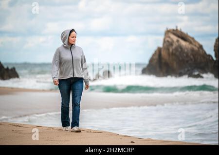 Portrait of happy smiling caucasian mature woman in jeans walking running at autumn fall day outdoor on shore beach at sunset, lifestyle natural emoti Stock Photo