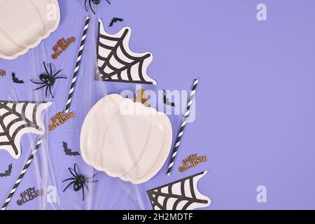 Halloween party flat lay with pumpkin shaped plate, spiders, bats and spiderwebs on violet background with copy space Stock Photo