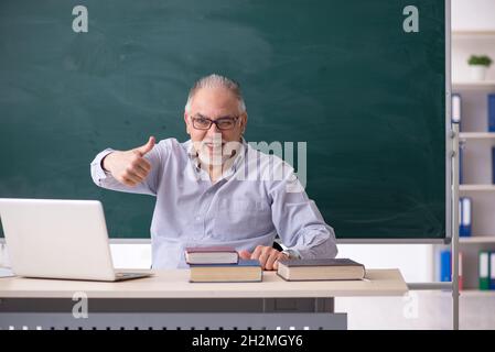 Old teacher in front of green board Stock Photo