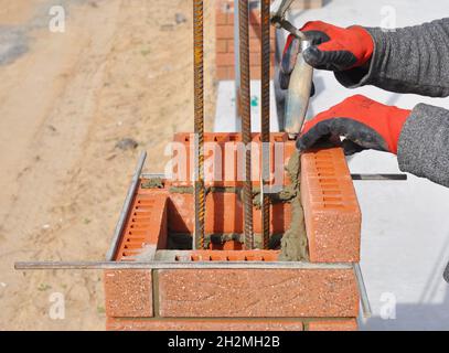 Bricklaying Closeup. Bricklayer hand holding a Putty Knife and Building a Brick Wall Column with Iron Bar Outdoor. Stock Photo