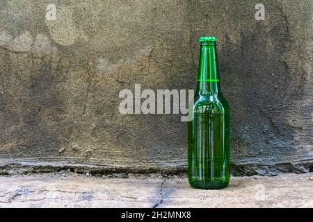 A closed bottle with an alcoholic drink stands against the wall. A bottle of beer forgotten on the street Stock Photo