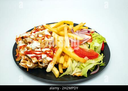 Donner kebab with chips and salad,  on a black plate isolated on white background. Stock Photo