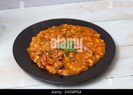 Beans with sausages on a black ceramic plate Stock Photo
