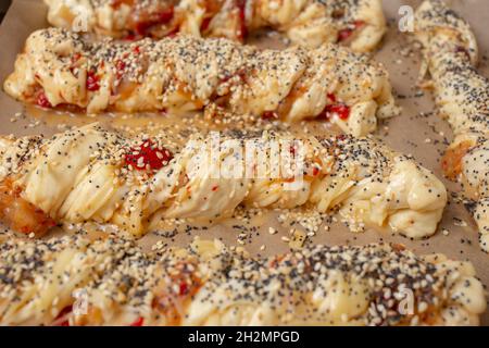twisted dough with pepperoni, poppy seeds and sesame seeds, on backing paper. Pizza with a twist. Stock Photo