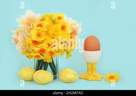 Easter egg themed Spring composition with decorated eggs, healthy brown breakfast egg in cute chicken eggcup, vase of daffodils Stock Photo