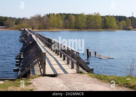 Old wooden vintage half destroyed pedestrian bridge with handrail over the lake Stock Photo