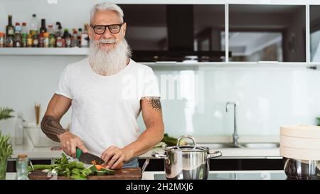 Happy senior man having fun cooking at home - Elderly person preparing health lunch in modern kitchen Stock Photo