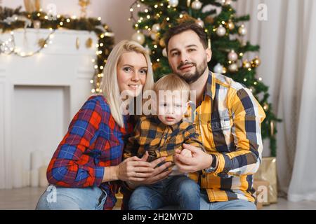 Happy family near christmas tree having fun on the floor. Christmas celebration at home. Mom, Dad and son weared in casual. Happy family funny playing Stock Photo