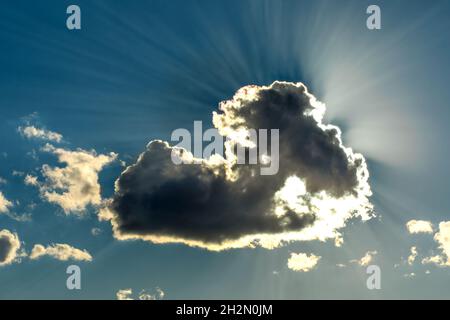 Sun is shining from behind clouds. Blue sky with clouds and sunbeams. Sun hidden behind a cloud. Stock Photo