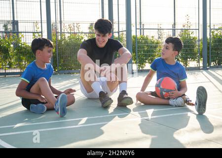 Three brothers sitting on the football court floor resting and talking. Stock Photo