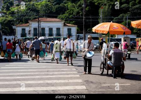 Salvador, Bahia, Brazil - June 29, 2019: Street movement in front of the São Joaquim fair in Salvador. Pedestrians cross and a man plays the tambourin Stock Photo