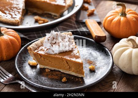 Slice of pumpkin pie with whipped cream and cinnamon with mini pumpkins in background Stock Photo