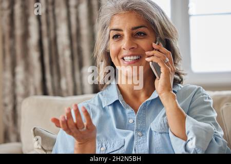 Smiling Mature Woman Making Call On Mobile Phone At Home Stock Photo