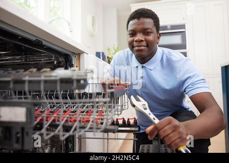 Portrait Of Young Man Training As Plumber Fixing Domestic Dishwasher In Kitchen Stock Photo