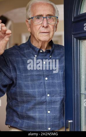 Portrait Of Anxious Senior Man At Home Looking Out Of Front Door Stock Photo