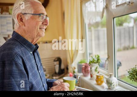 Smiling Senior Man Looking Out Of The Window Holding Cup Stock Photo