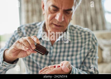 Mature Man Sitting On Sofa At Home Taking Medication Pills From Bottle Stock Photo