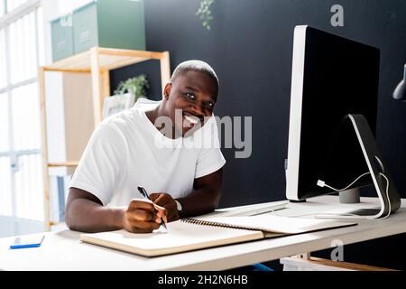 Male freelancer writing in spiral notebook at desk in studio Stock Photo