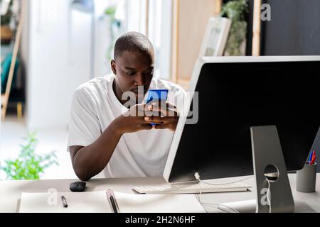 Male freelance worker touching desktop screen while sitting at desk in studio Stock Photo