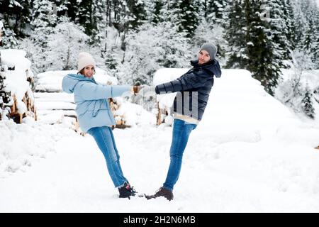 Playful couple holding hands while enjoying hike in forest during snowfall Stock Photo
