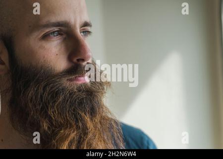 Thoughtful man with brown beard in front of wall Stock Photo