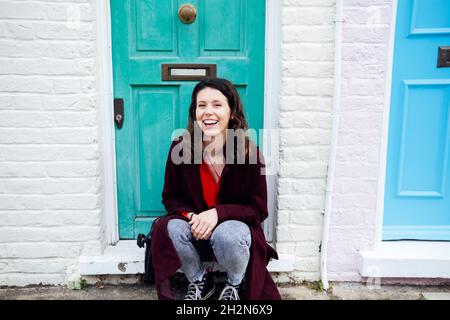 Cheerful young woman sitting on doorstep Stock Photo