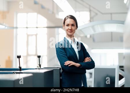 Confident female professional standing with arms crossed in industry Stock Photo