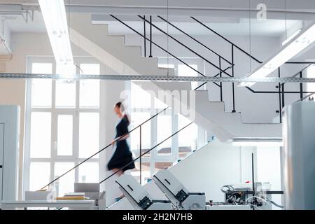 Businesswoman moving down on staircase in workshop Stock Photo